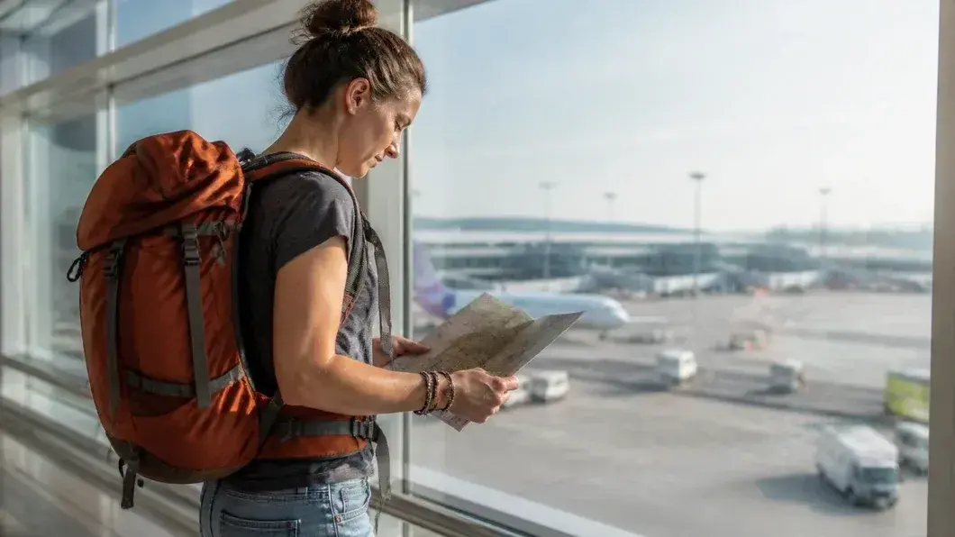 Une voyageuse avec un sac de randonnée consulter une carte près d'une grande fenêtre d'aéroport